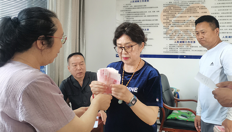 头题片，5月30日，某药业公司按协议约定完成第一期履行义务，将十万现金交到法院，调解员付菊（左一）清点无误之后交到农民工委托代理人徐某手中