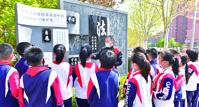 头题图,普法志愿者在宪法墙前给学生们普及法律知识。