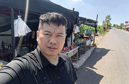 姜立伟在城郊的水果摊前完成工作打卡（图片由受访者提供）